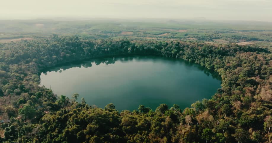A large round lake is completely surrounded by a dense collection of trees
