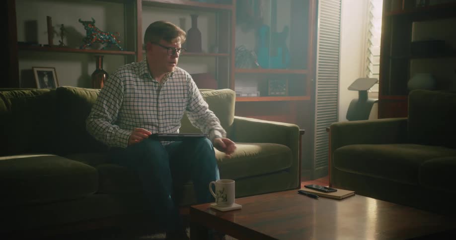 Man sitting on couch in living room closes laptop and picks up smartphone