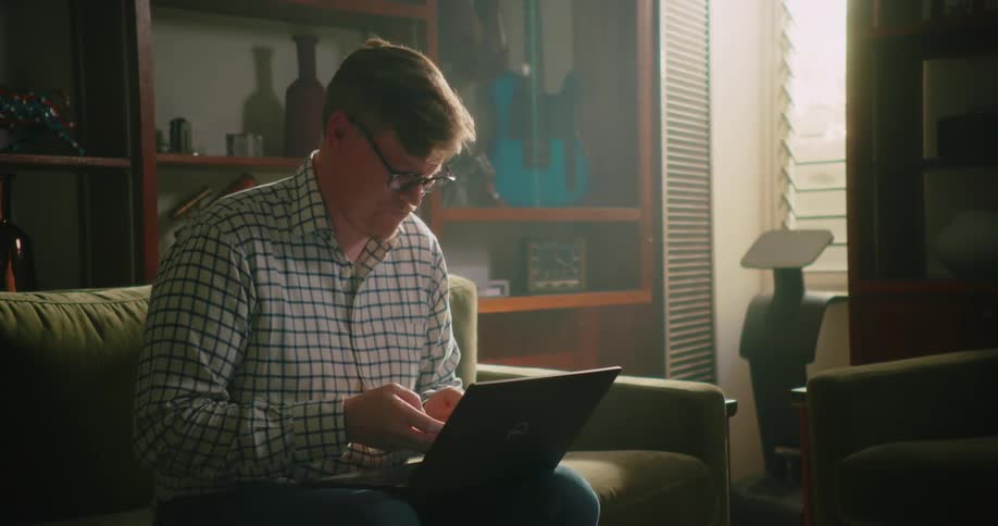 Man working on laptop at home stops to text on smartphone