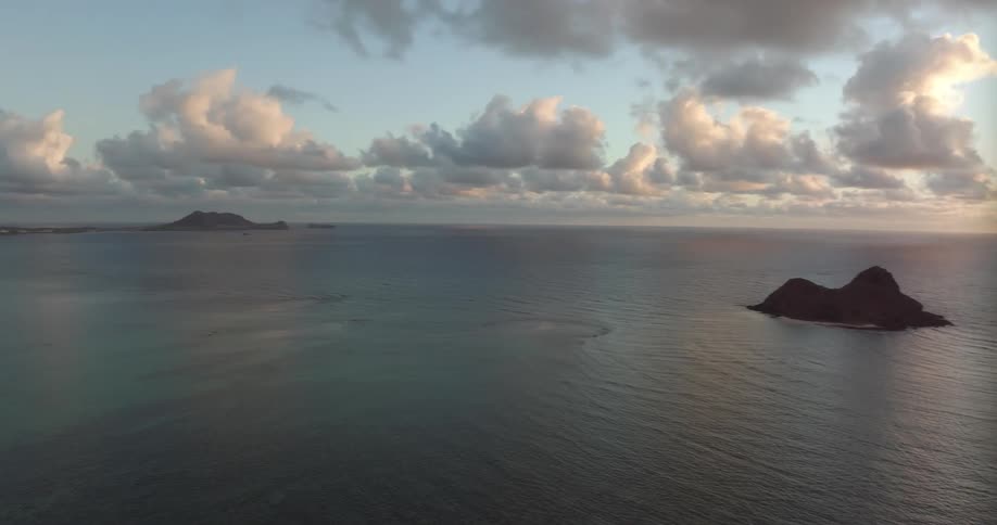 Sun shining on horizon illuminates concentric ripples flowing around islands a short distance from town on shore
