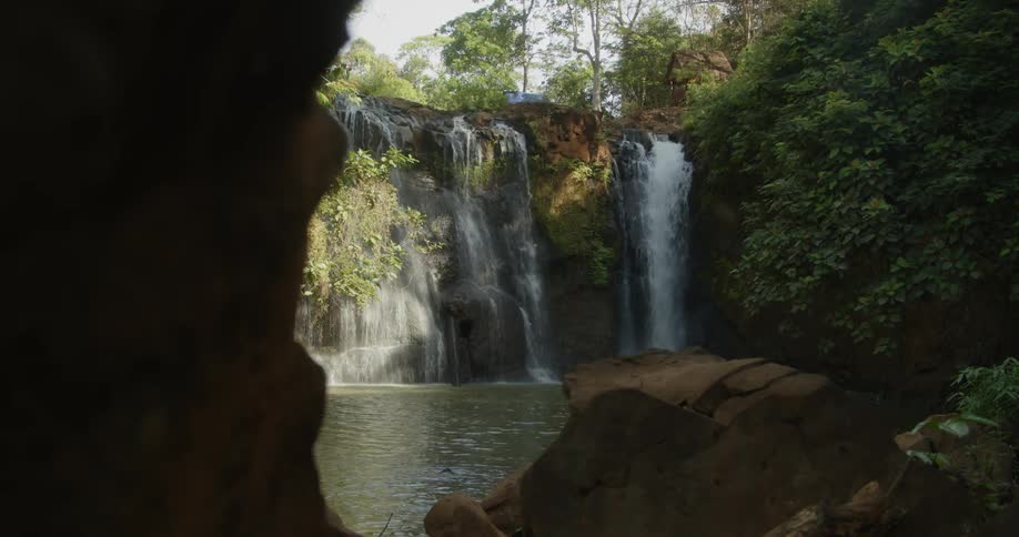 Multiple waterfalls flow into pond at base of cliffs near cavern