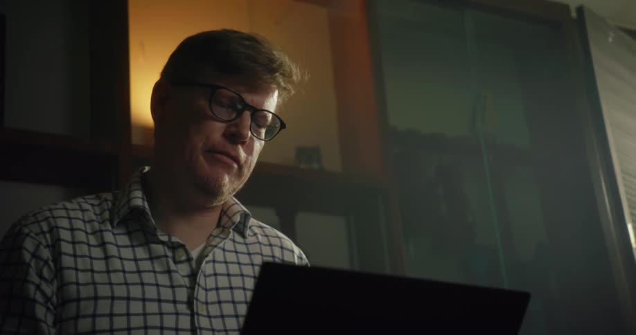 A man is sitting down with a laptop computer and talking as he types