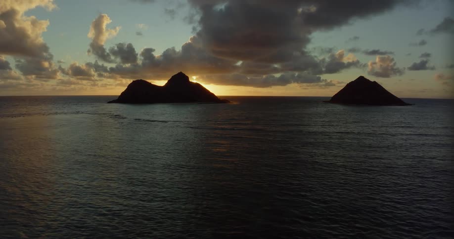 Sun shines from red sky on horizon casting islands into silhouette