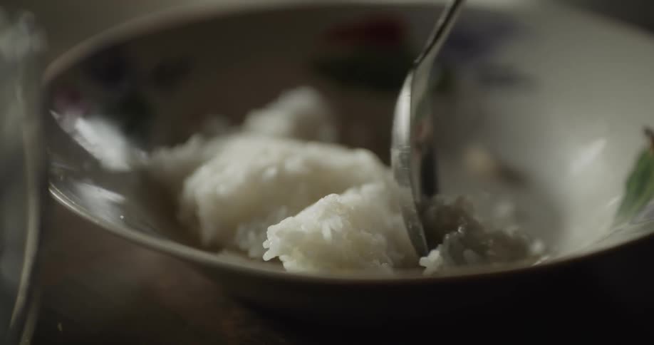 A hand picks up a spoonful of sticky rice from a patterned bowl
