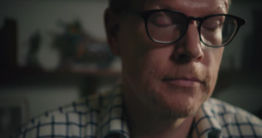 A man wearing glasses looks up from he is working on to think and then he looks back down
