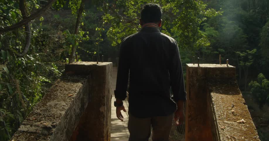 A man walks across a rope bridge in the woods