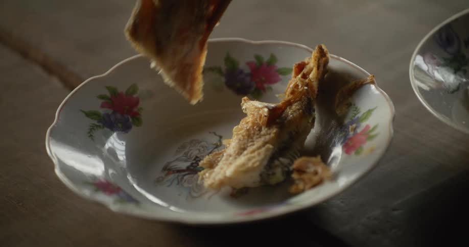 A hand picks up a piece of fried food from a patterned bowl