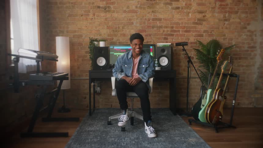A teenage male sits in a room with musical instruments while laughing at something