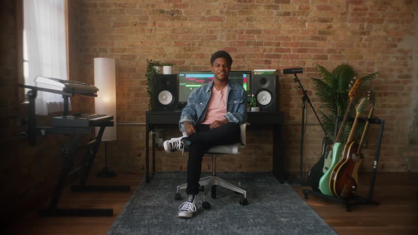 Man sits back smiling in chair near computer between musical instruments