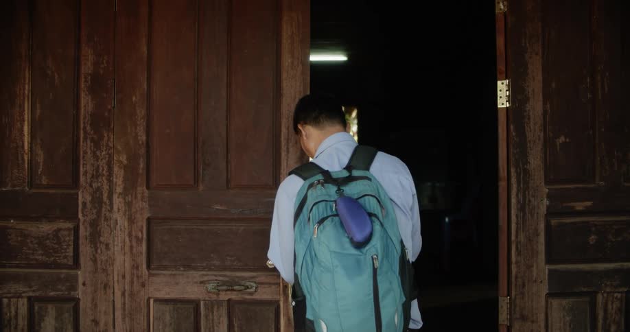 Man unlocks and opens wooden door to building showing window on other side of the room
