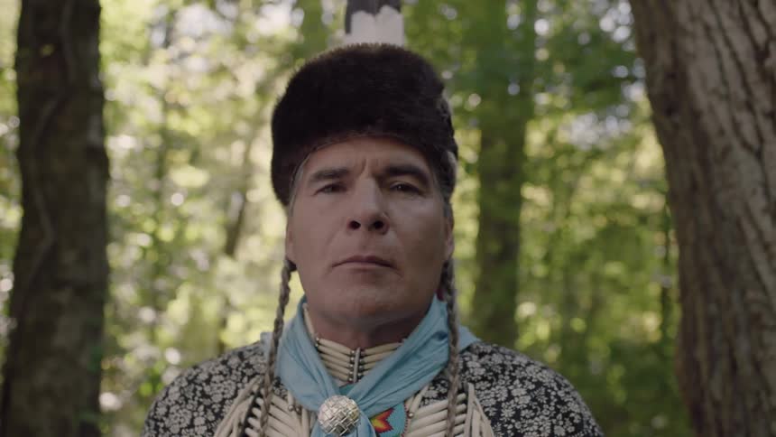A native american man in ceremonial attire opens his eyes