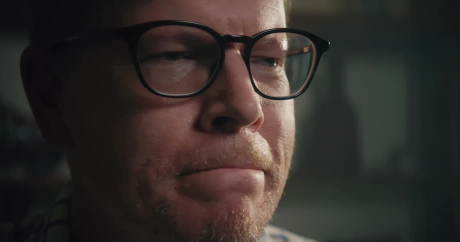 A man wearing glasses looks up from what he is working on and shakes his head