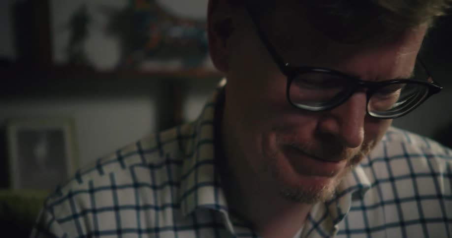 A man wearing glasses is sitting at a table talking and using his hands when he expresses himself