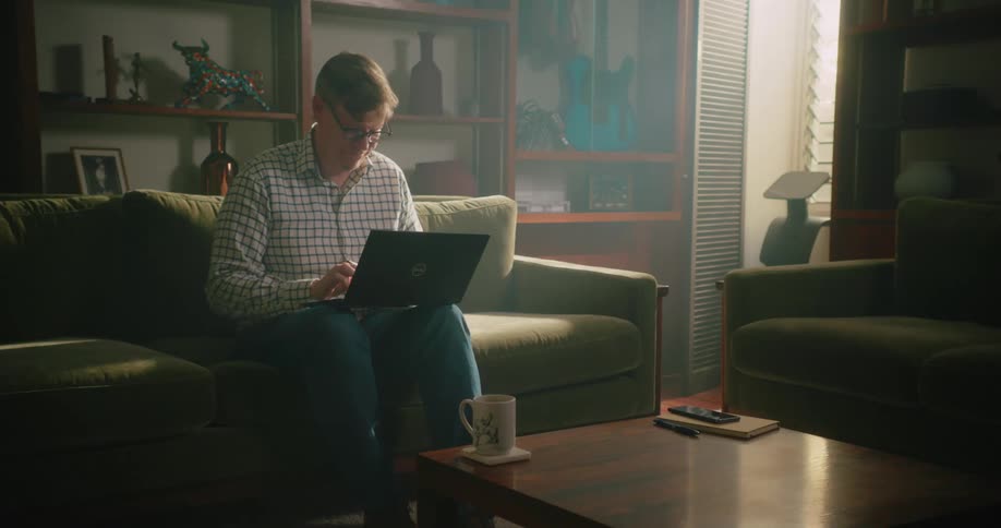 A man sits on the couch with his laptop in his lap