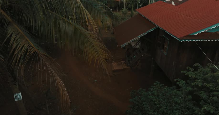 Red roofed building standing on pilings sits in village surrounded by jungle