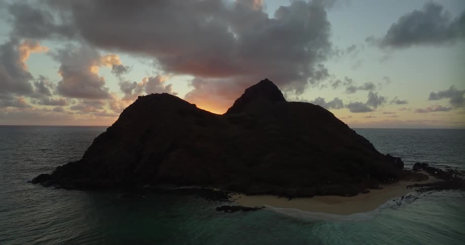 Island is back lit by sun sitting on horizon over the ocean