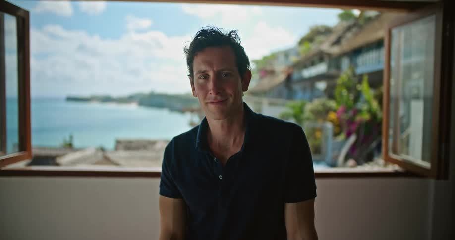 Man sits near window showing scenic seaside town and ocean