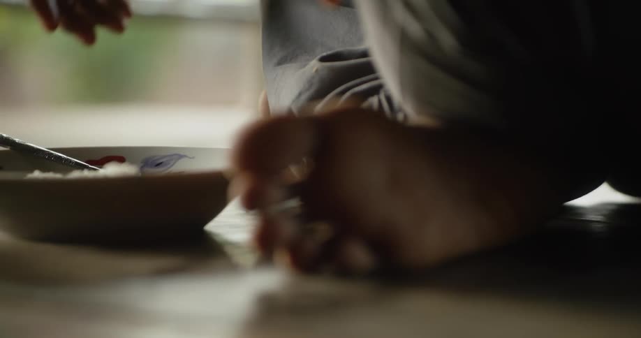 A close up of a mans feet are shown as he sits crossed legged on the floor eating rice out of a bowl