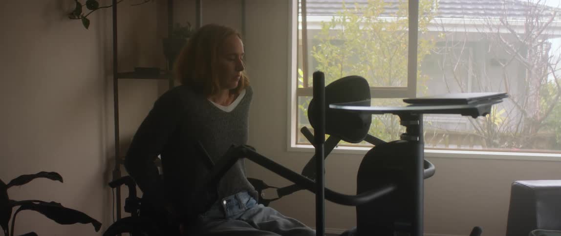Woman in wheelchair uses lift to get into position facing laptop