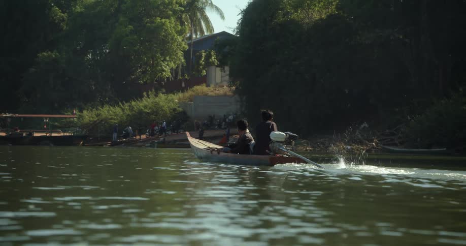 Two people drive a boat towards the shore where a group of people are
