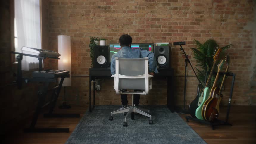 Musician turns chair toward computer in work area with keyboard and guitars