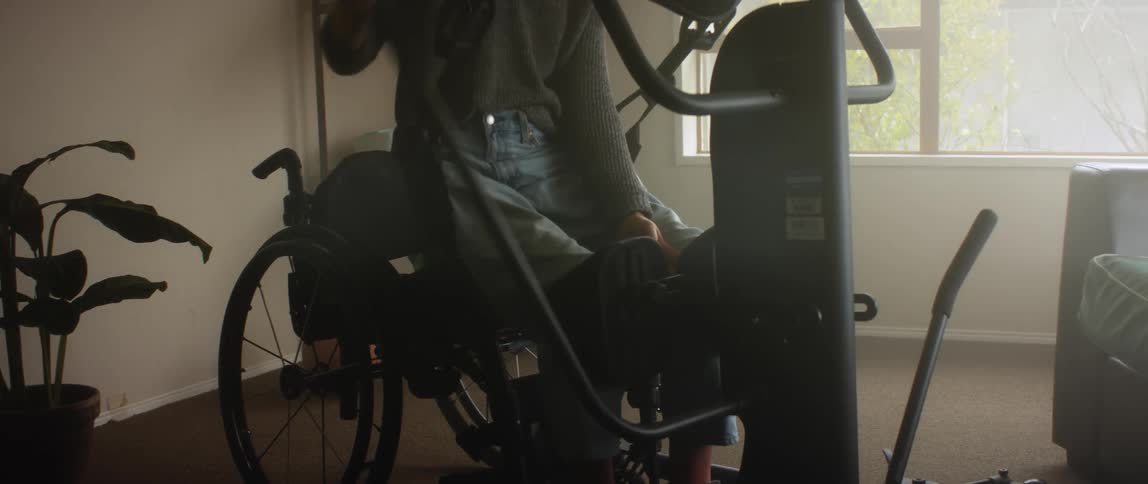A woman sits on an exercise bike while repeatedly pulling a lever that raises the front end of it