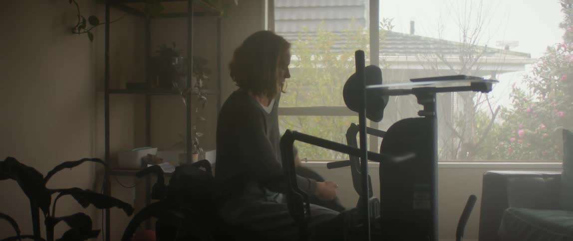 Woman in wheelchair rolls forward and uses machine in living room