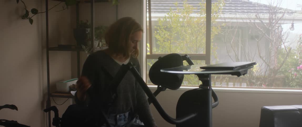 A woman is sitting at an exercise machine in her home and pulling a lever on the side to raise the bars