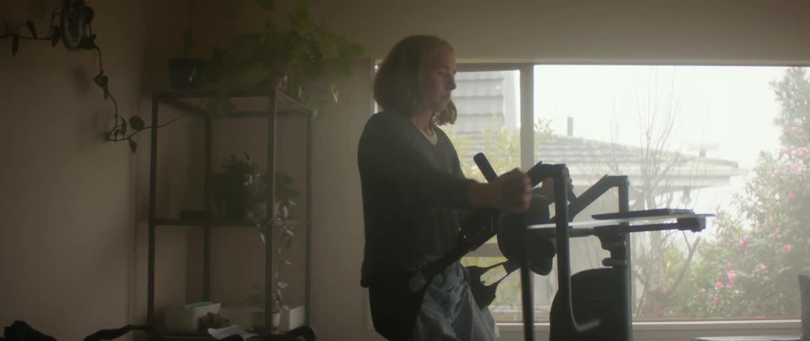 Woman uses sling lift to move upright from wheelchair in living room