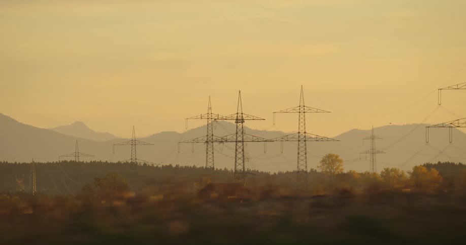 Power lines and transmission towers stretch across the land below tall mountains