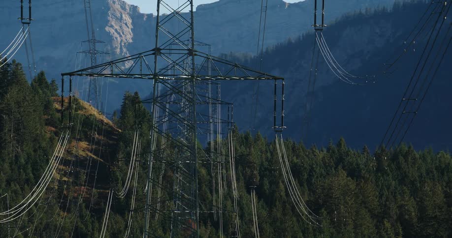 A series of transmission towers spanning a forested mountain range during the day