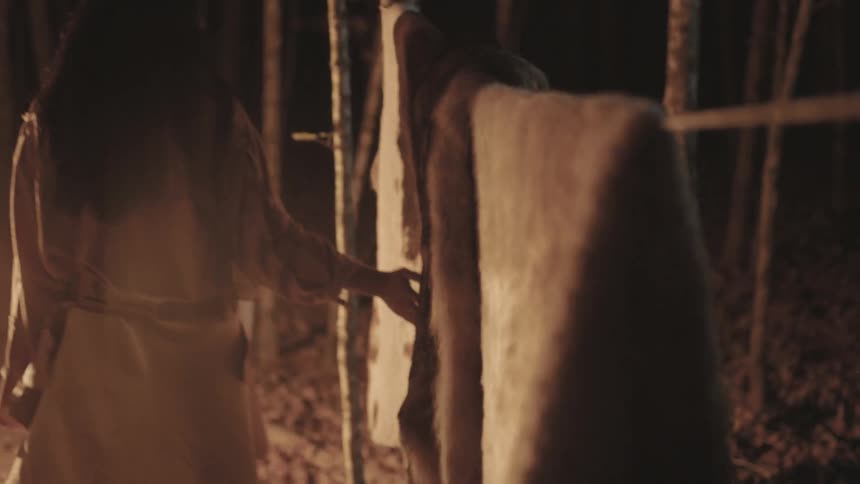 A woman running her fingers across pelts hung on a line near a fire