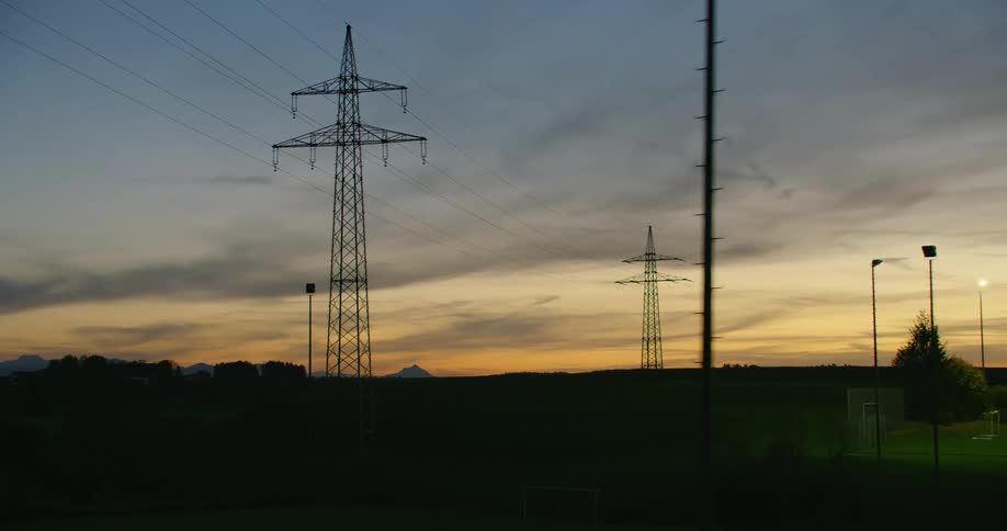 Transmission towers stand tall above trees as power lines stretch across the sky near a park