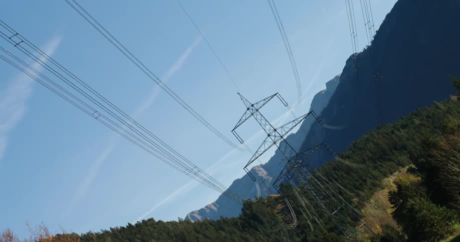 Transmission towers and cables running through a field by a forest and hills