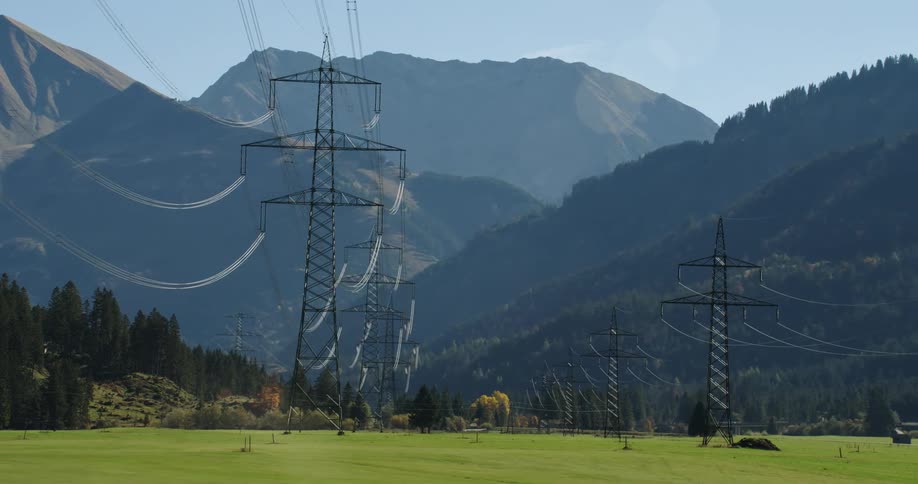 Transmission towers stand tall above trees as power lines stretch across the sky in a mountain valley
