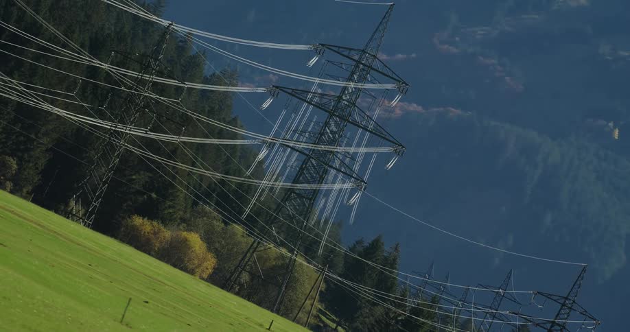 Transmission towers stand tall above trees as power lines stretch across the sky over a forest with mountains in the distance