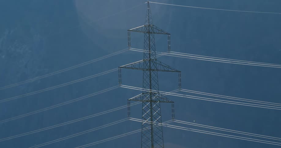 Large electric transmission tower connected to many power lines stands over park near woods