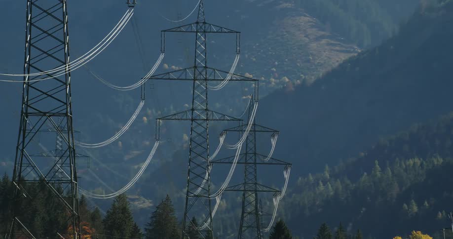 Multiple transmission towers on the slopes of mountains covered in pine tree forests