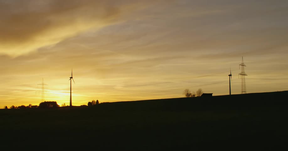 Wind turbines loom over a hill in the countryside at sunset