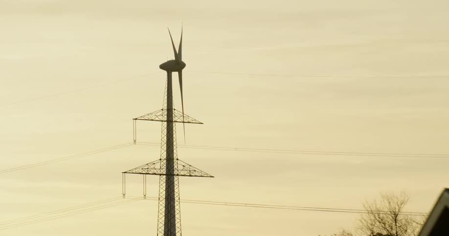 A wind turbine spins next to an electrical tower