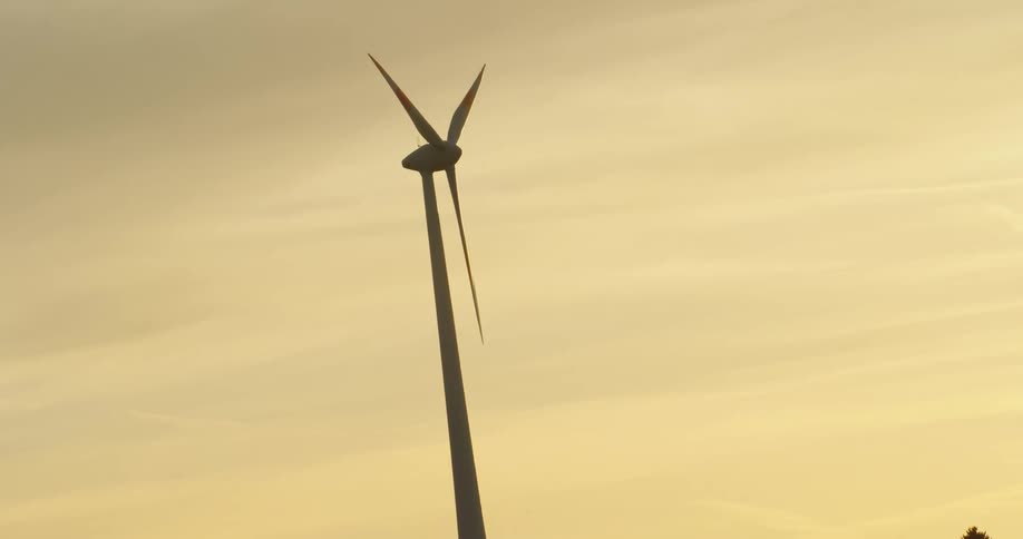 Twisting footage of a wind turbine spinning on the countryside at evening