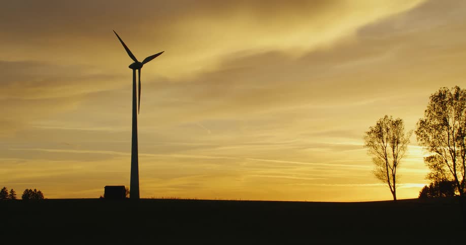 A wind turbine slowly spins in the countryside at sunset