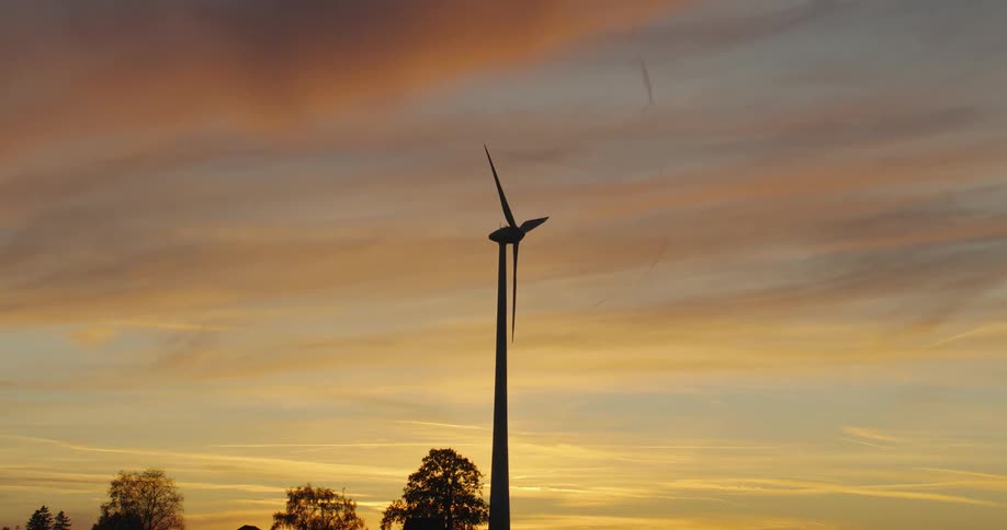 Blades on wind turbine silhouetted against red sky turn slowly