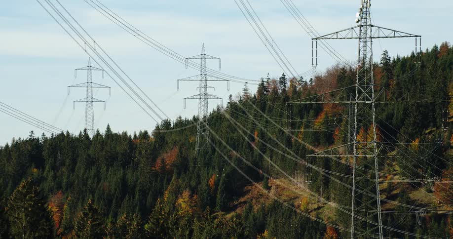 Power lines stretch above trees and across electrical utility towers in forested mountains