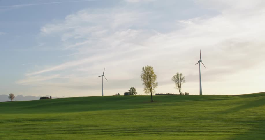 Bright sun shines from horizon over rotating wind turbines with mountains in the distance