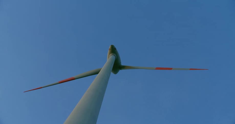 A wind turbine spins high in a clear blue sky