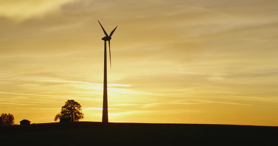 Rotating wind turbine and buildings are silhouetted against cloudy red sky