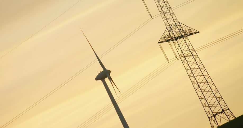 The blades spin slowly on a windmill near a power line tower