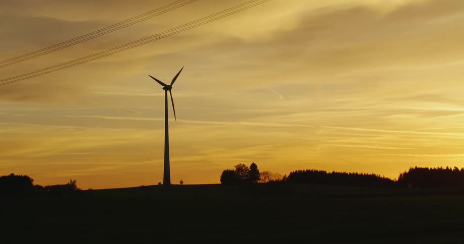 Wind turbine is silhouetted against the sky at sunset
