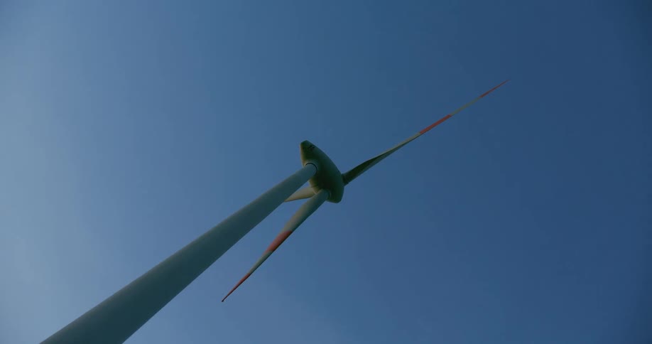 Striped wind turbine blades rotate slowly under a blue sky